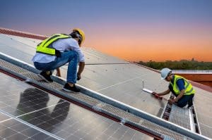 Two workers in safety gear install solar panels on a roof at sunset, using tools and equipment to secure the panels in place—experienced Solar Installers Plaquemines Parish trust for quality workmanship.