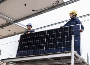 Two workers in helmets, part of the skilled Solar Installers in St. Bernard Parish, install a solar panel on scaffolding beneath a large metal structure.
