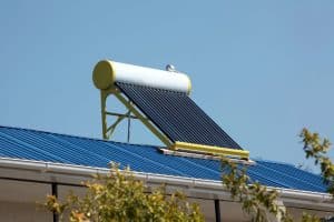 A Solar Water Heater with black vacuum tubes and a white tank is installed on a blue metal roof under a clear sky.