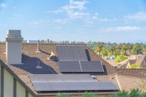 Rooftop solar panels on a residential house in a suburban California neighborhood with trees and blue sky in the background, highlighting the growth of solar in California.