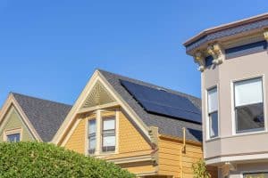Yellow house with solar panels installed on its roof, showcasing solar in California, next to a beige house with decorative trim, both under a clear blue sky.
